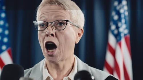 Woman Speaking at a Press Conference with Flags