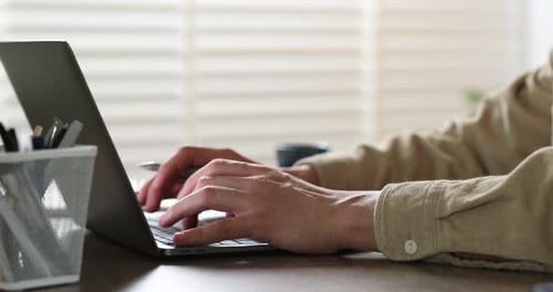 Man working on laptop at wooden desk in office, closeup