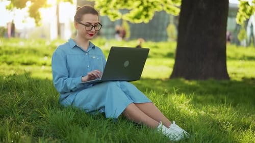 Busy Attractive Woman Working at the Laptop As Sitting on Grass in City Park