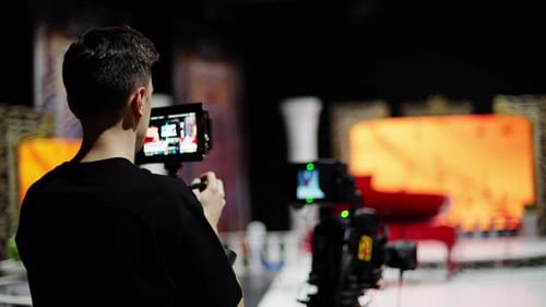 Cameraman Monitors Video Camera Settings in Studio