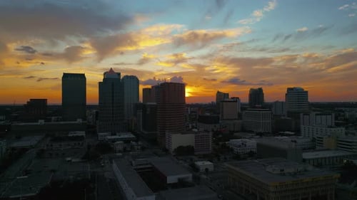 Horizonte de Tampa ao pôr do sol com céu amarelo brilhante e edifícios em silhueta, rastreamento aéreo até o