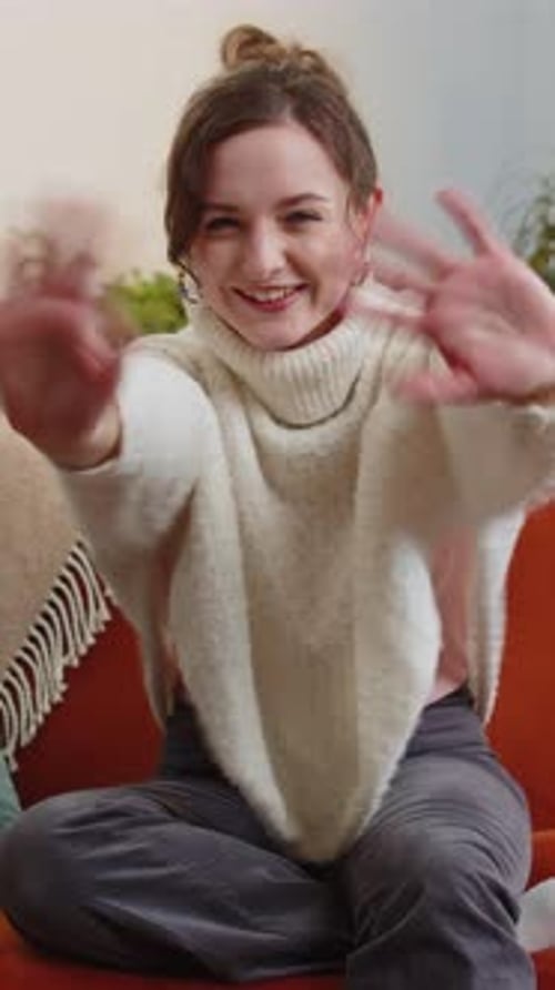 Hübsche Frau lächelt freundlich in die Kamera und winkt mit den Händen und gestikuliert Hallo Hallo Gruß zu Hause auf dem Sofa
