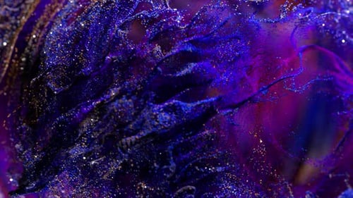 Goldene und blaue Partikel vermischen sich in einer violetten Flüssigkeit und erzeugen wunderschöne Wirbelmuster und