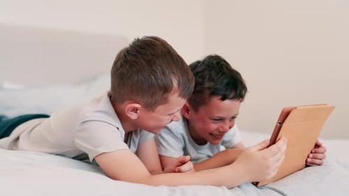 Two Boys Laughing Together While Using Tablet