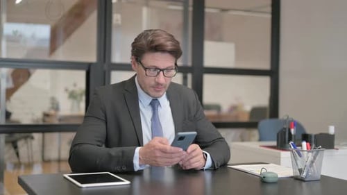 Middle Aged Businessman using Phone while Sitting in Office