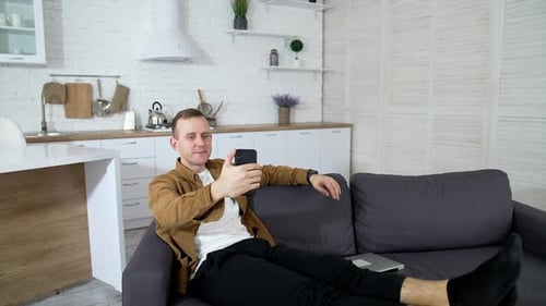 Young Man Lying on Sofa Using Phone