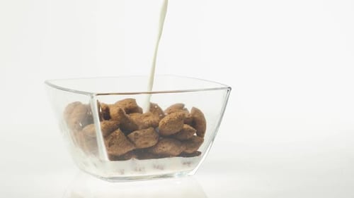 Fresh healthy food. Milk pouring into transparent bowl with chocolate cereal pads on a background