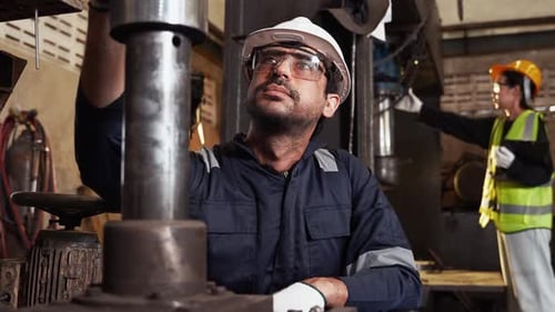 Industrial engineer in a hard hat and safety glasses inspecting heavy machine with a wrench