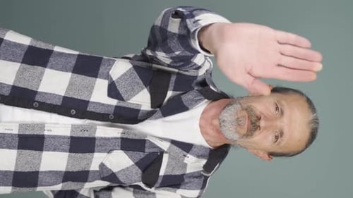 Vertical video of Old man making stop sign for camera.