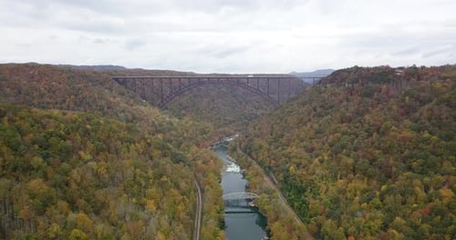 Slow aerial dolly of cars driving along the River Gorge Bridge with autumnal trees
