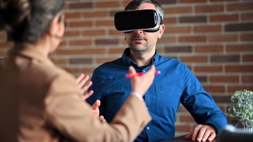 Man using a Virtual Reality headset in an office while woman explains and gesticulates