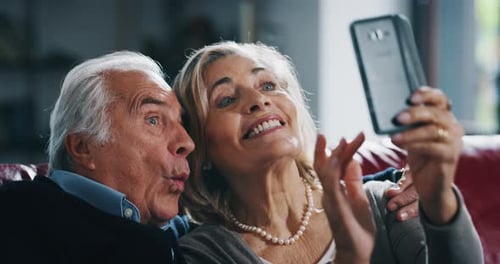Close up of happy mature senior couple is taking selfie with a smartphone in living room.
