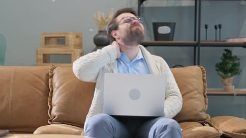 Man Rubs Neck While Using Laptop at Home