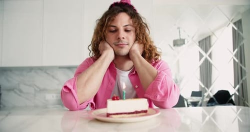 Calm Man in Festive Birthday Hat Sitting at Home Looking at Cake with Candle Feeling Frustrated
