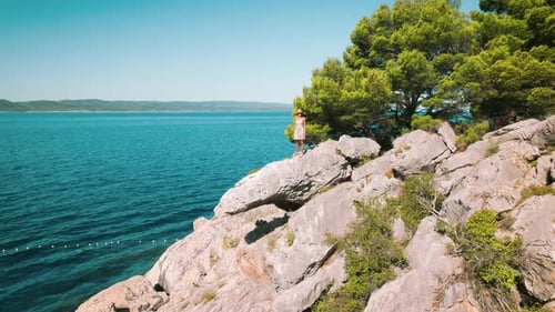 Perched on the edge, a girl gazes out over the serene Adriatic Sea. Female stands alone amidst natur