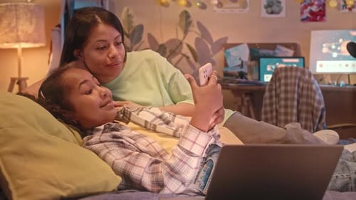 Girl and Adult Viewing Smartphone on Bed