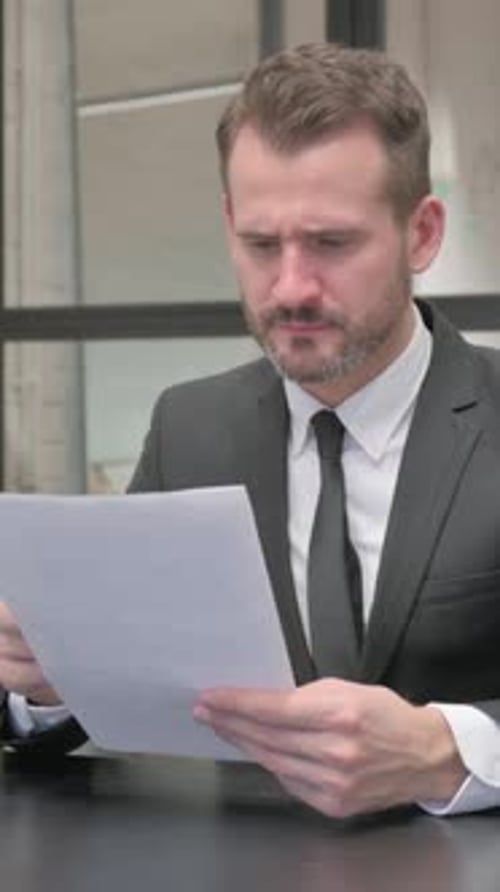 Professional Man Reviews Documents at Desk in Office