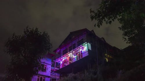Time-Lapse of Clouds amidst Starry Sky at Night over an Illuminated House.