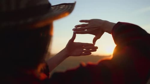 Woman Framing Sunset with Fingers in Rural Setting