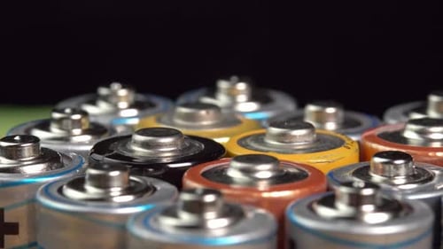 Rows of used alkaline AA batteries rotate on black background. Lithium ion battery pack close up