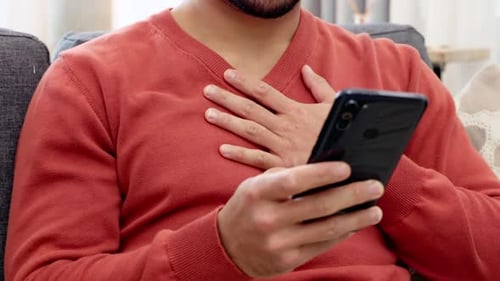 Heart attack, emergency and pain with man holding his chest while sitting on his living room sofa