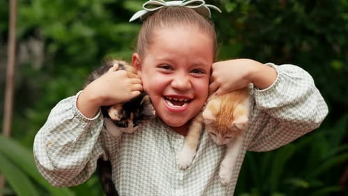 Cute little happy blonde latina girl with a big smile stroking playing with two pet kitten