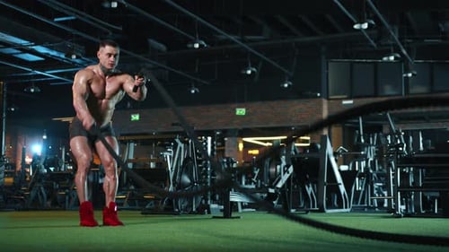 Muscular Man Exercising with Battle Ropes at Gym