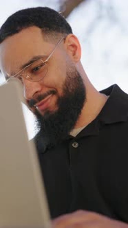 A Man is Engaged in Working on His Laptop While Enjoying the Great Outdoors and Wearing Glasses