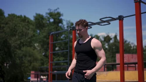 young athlete bodybuilder standing on the sports field after outdoor training takes off his shirt