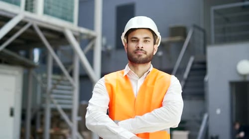Portrait of smiling professional engineer wearing safety helmet and vest standing at factory with