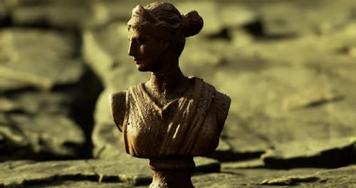 Sculpture of a Woman in Classical Attire on a Rocky Surface in Natural Light