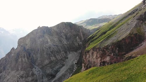 The Stark Contrast of a Rugged Mountain Cliff Face with Patches of Green Vegetation Showcasing the