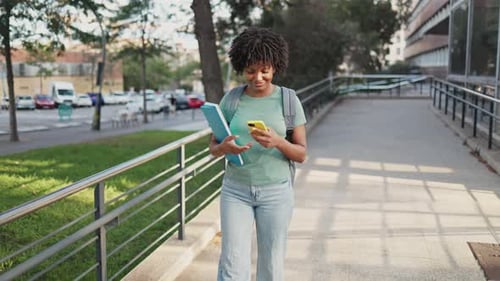 Young student using smartphone while walking on campus pathway