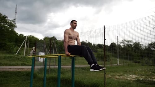 Muscular Man Doing Leg Raises on Parallel Bars