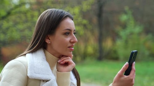 Beautiful young outdoor communication. Pretty lady with phone sitting in park.