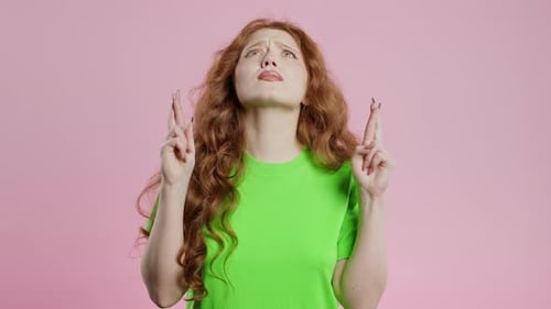 Red Haired Young Woman Praying with Crossed Fingers on Pink Background Lady Begs Someone Satisfy