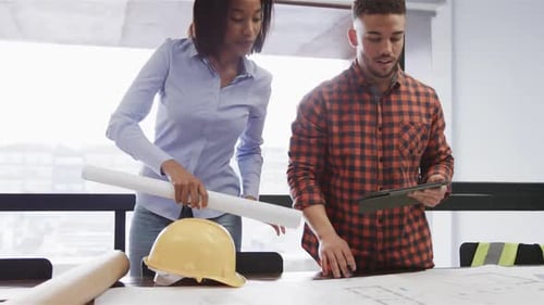 Diverse male and female architects with tablet discussing blueprints standing in office, slow motion