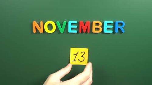 Hand sticking a sticker 13 November calendar day on school board. 13 date of November. Thirteenth