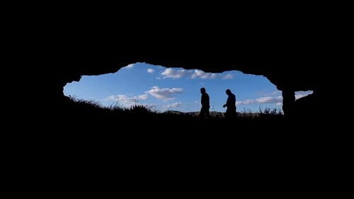 People Walking In Front Of An Ancient Cave