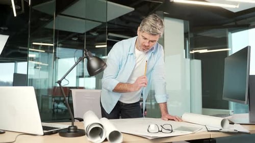 mature creative designer, architect working in the office at work a computer desk with drawings.