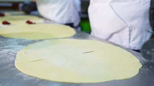 Baker verwendet ein Pizzamesser, um auf dem Tisch gerollten Teig zu schneiden. Nahaufnahme.