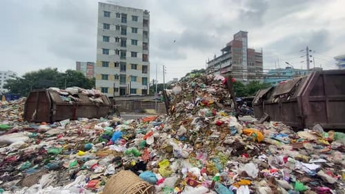 Pile Of Street Garbage Beside Road In Bangladesh. Pan Right To Reveal River Waterway
