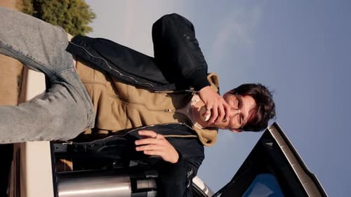 A young guy sits in the trunk of an SUV in the steppe and drinks tea from thermos admiring nature