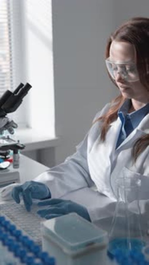 Female Scientist Conducting Research in a Modern Laboratory Setting Using Laptop and Test Tubes