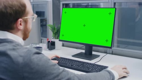 Over the Shoulder Shot of Motivated Businessman Working on Green Mock-up Screen Desktop Computer in