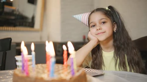 Uma jovem comemora seu aniversário com um bolo e velas coloridas usando um chapéu de festa e
