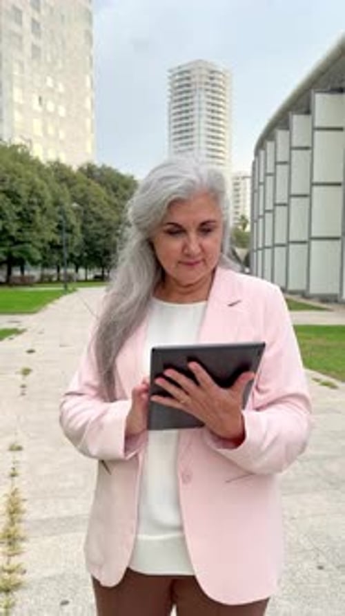 Elegant senior businesswoman using tablet computer in city park