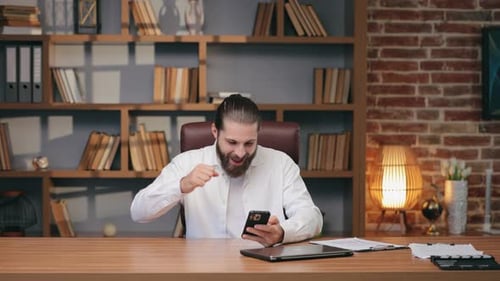 Man Celebrates Success While Using Smartphone in Office