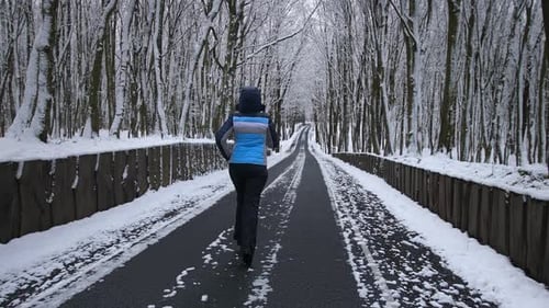 A Woman Runs Along a Forest Road The Trees are Covered with Snow on the Way of the Icicles