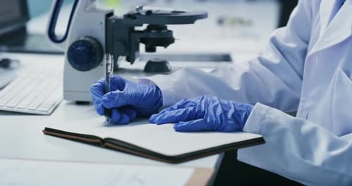Scientist Looks Through Microscope and Writes Notes